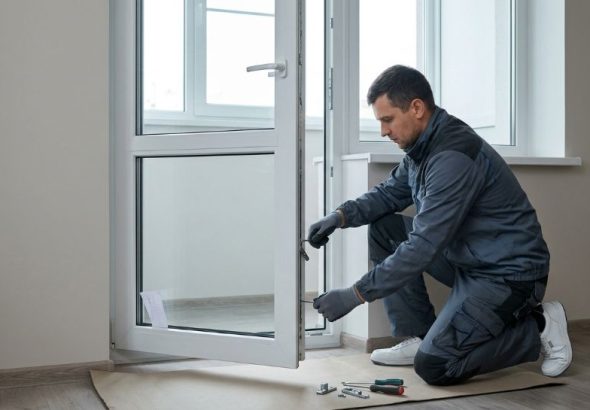 A technician adjusts a white PVC balcony door's lower hinge.