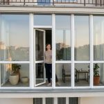 A woman stands inside a modern, floor-to-ceiling glazed balcony.