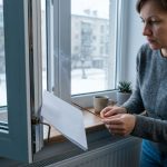 Жінка перевіряє протяг у пластиковому вікні аромапаличкою та папером.